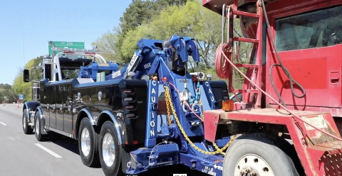 A Peterbilt tandem-steer Century 9055 wrecker towing a cement mixer on the highway.