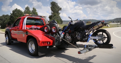 Image of a motor cycle being towed by a light-duty autoloader tow truck using the motorcycle attachment available from Miller Industries.