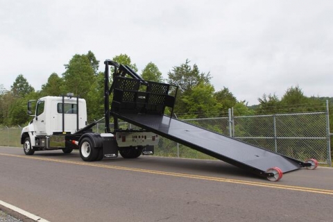 Image of the deck of a Titan C Series rolloff truck rolling backward to off load the deck onto the ground.